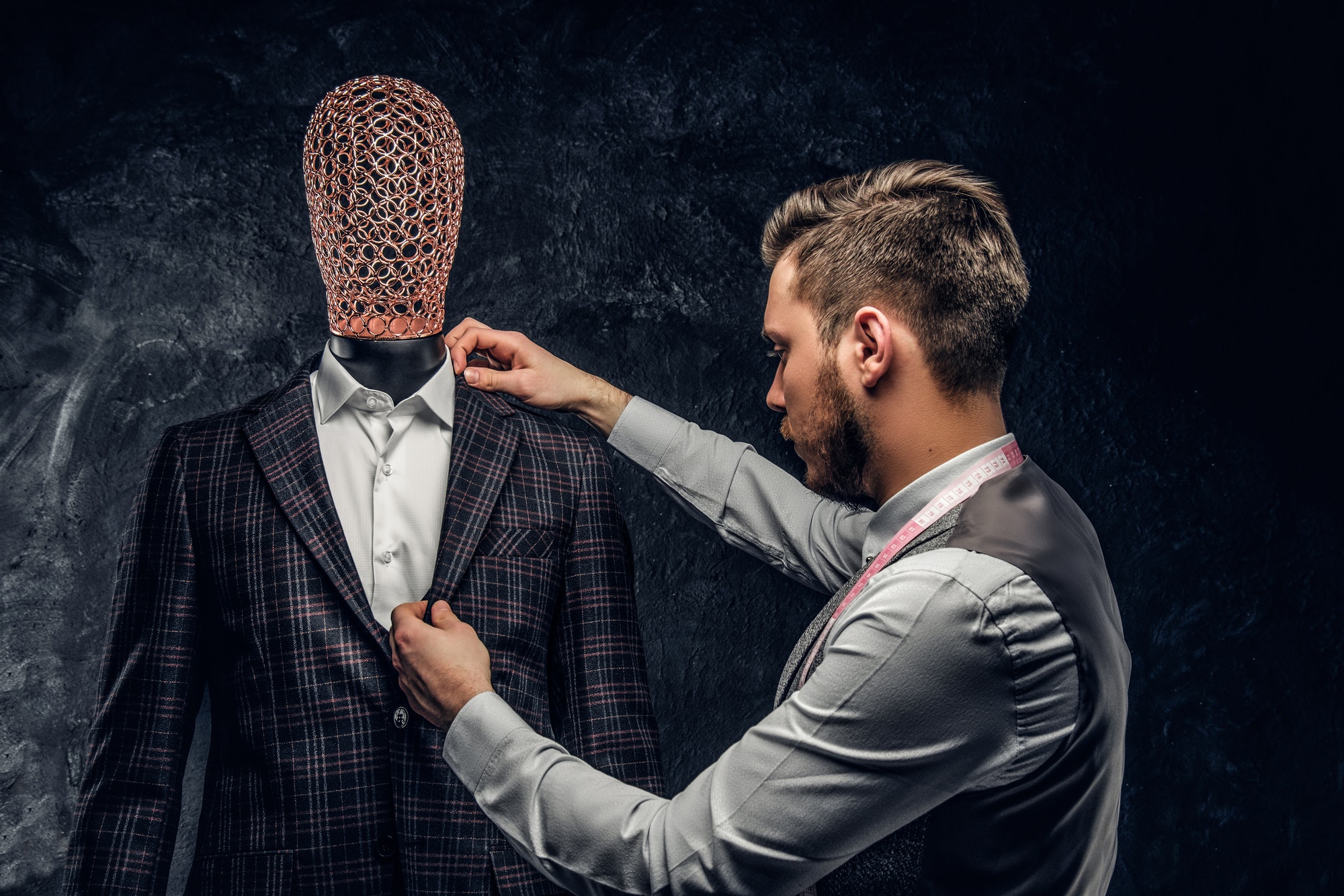 Young fashion designer next to a mannequin in exclusive custom made suit in a dark tailor studio